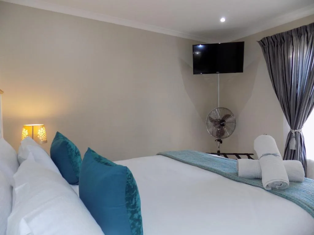 Modern bedroom with white bedding, teal accent pillows, wall-mounted TV