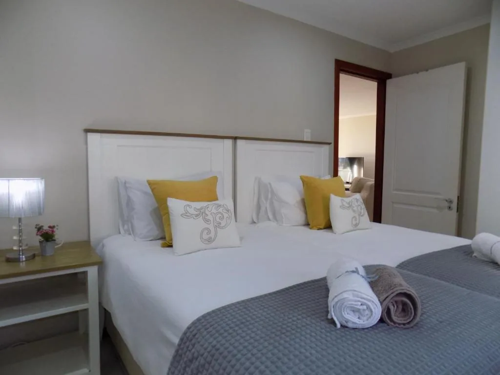 Bright bedroom with twin beds, yellow cushions, and fresh towels displayed