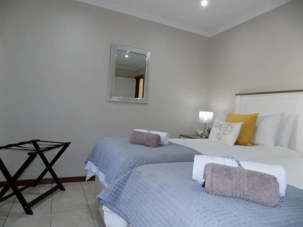 Twin beds with blue quilts, yellow pillows, and rolled towels in bright room