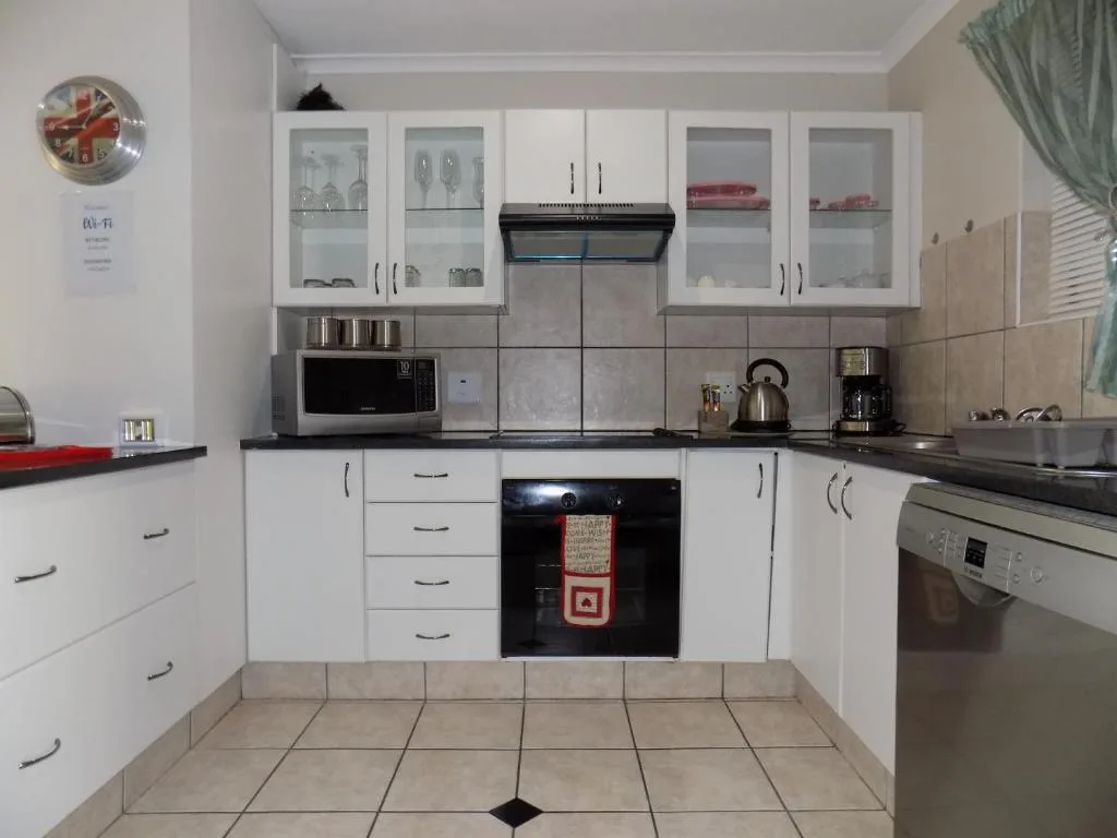 Modern white kitchen with black countertops, stainless steel appliances, and tiled flooring