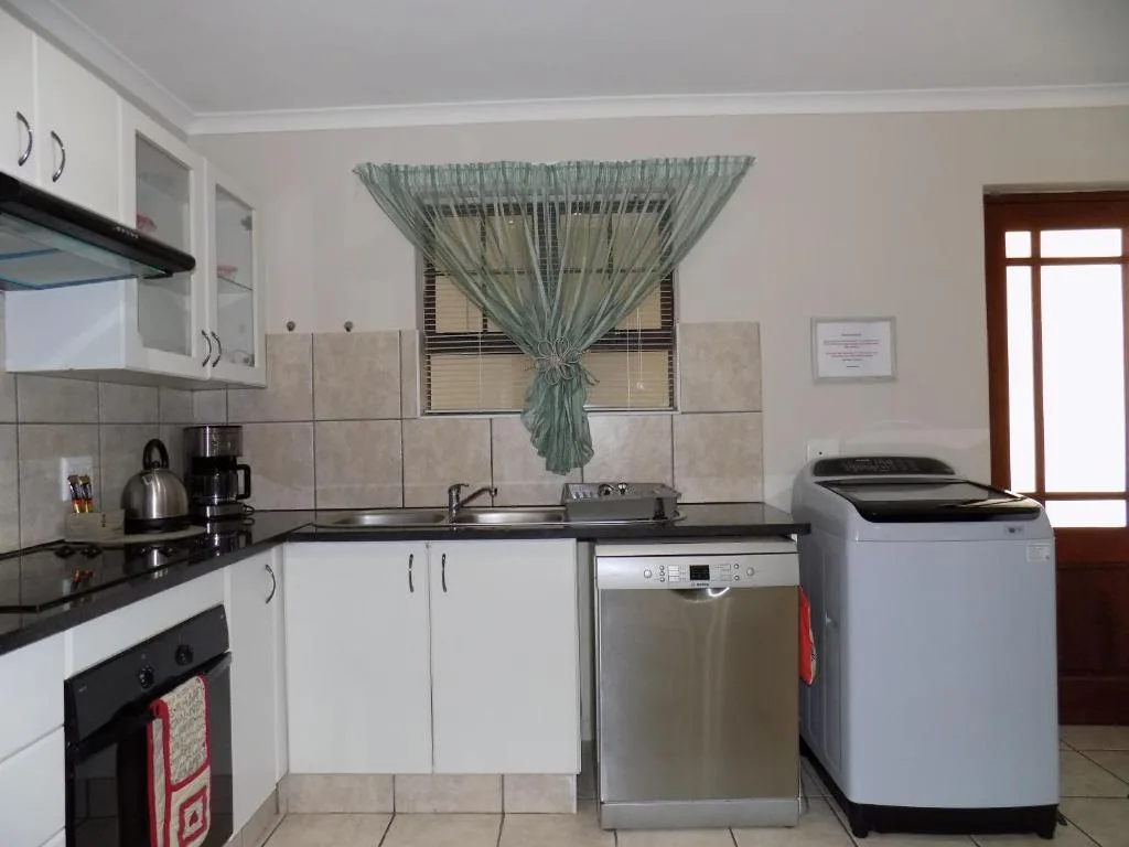 Modern kitchen with white cabinetry, black countertop, stove, dishwasher, and washing machine
