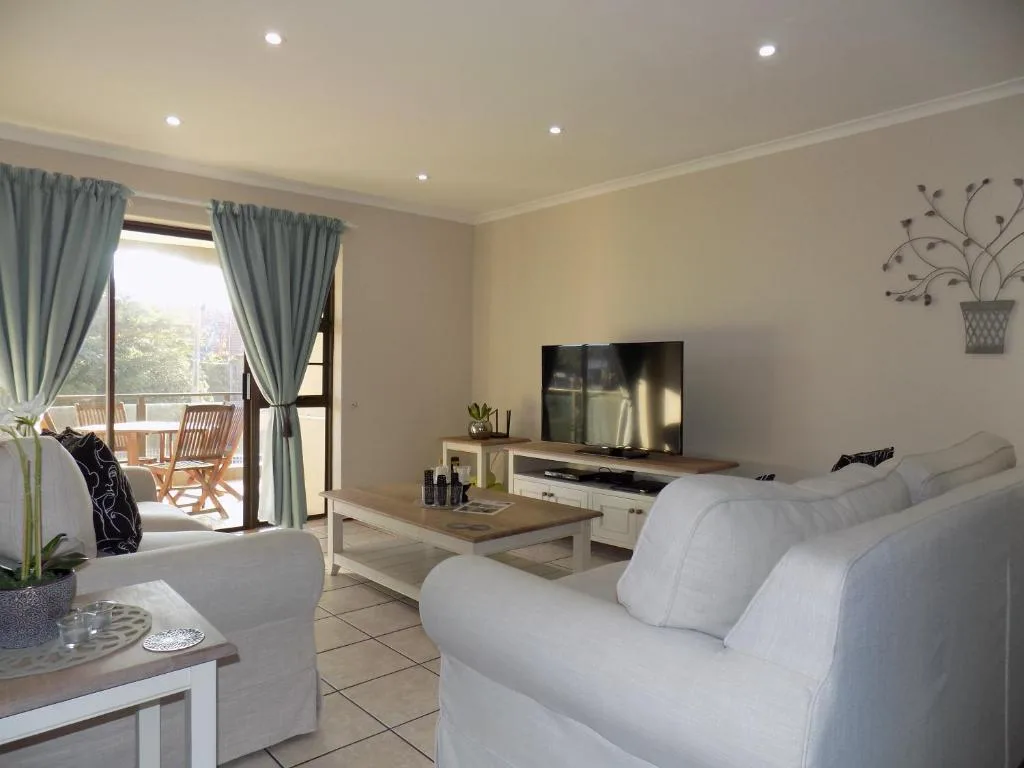 Bright living room with white sofa, TV, and deck access overlooking garden