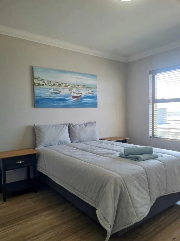 Bright bedroom with neatly made bed and coastal artwork above headboard