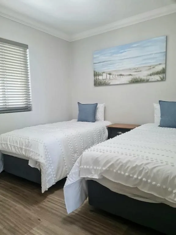 Twin bedroom with white quilts, blue pillows, and coastal artwork