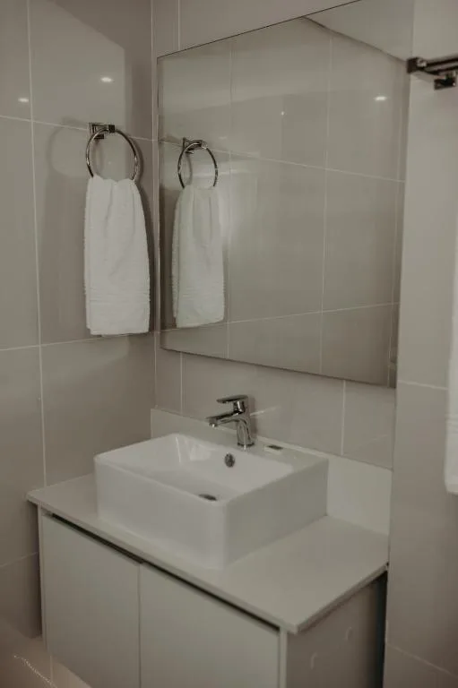 Modern bathroom with white vanity sink, mirror, and rolled towels