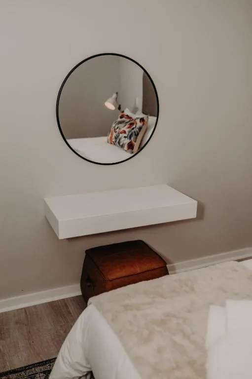 Bedroom with floating white shelf and round mirror above wooden stool
