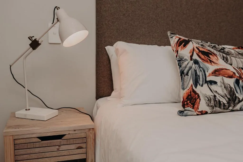 Bed with white linens and patterned pillow beside wooden nightstand with lamp