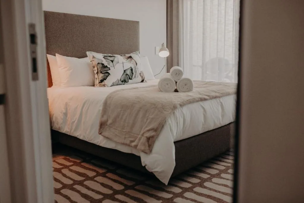 Elegantly styled bed with white linens and patterned pillows, fresh towels included