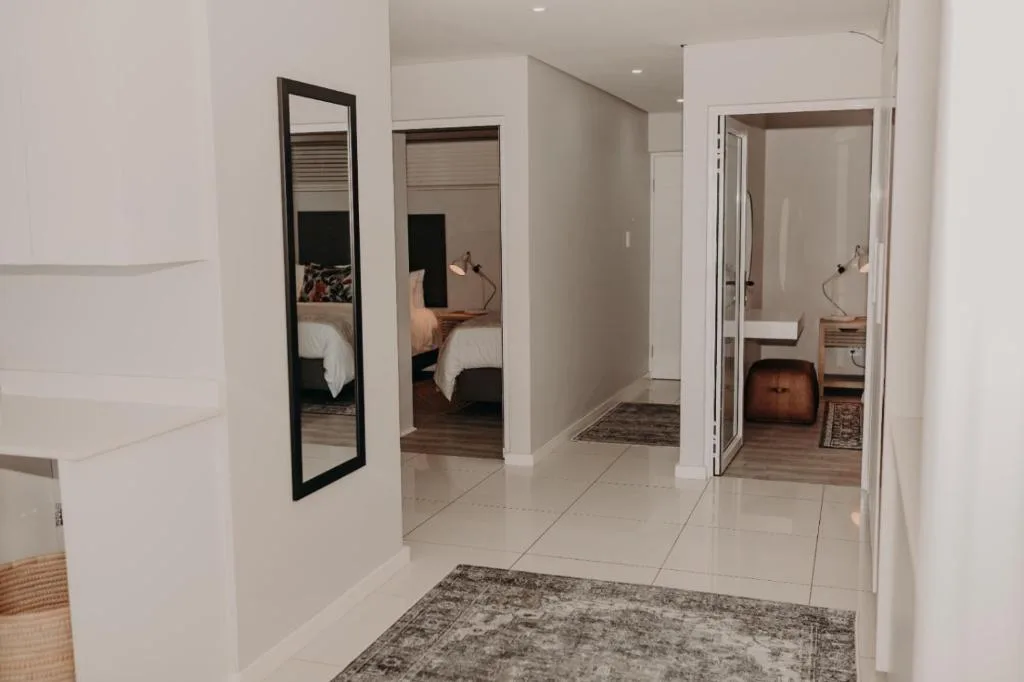Modern hallway with white walls, tile flooring, and mirror doors leading to bedrooms