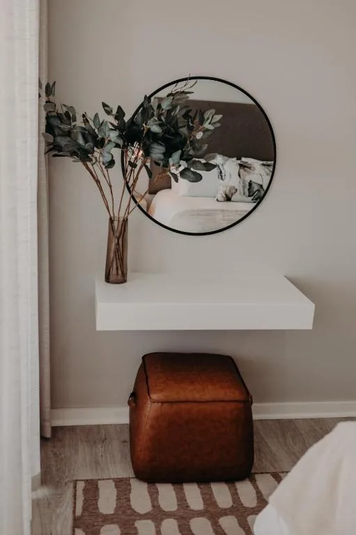 Stylish bedroom corner with round mirror, dried flowers, and leather pouf