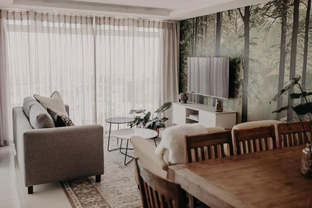 Modern lounge with gray sofa, TV, and forest wallpaper accent wall