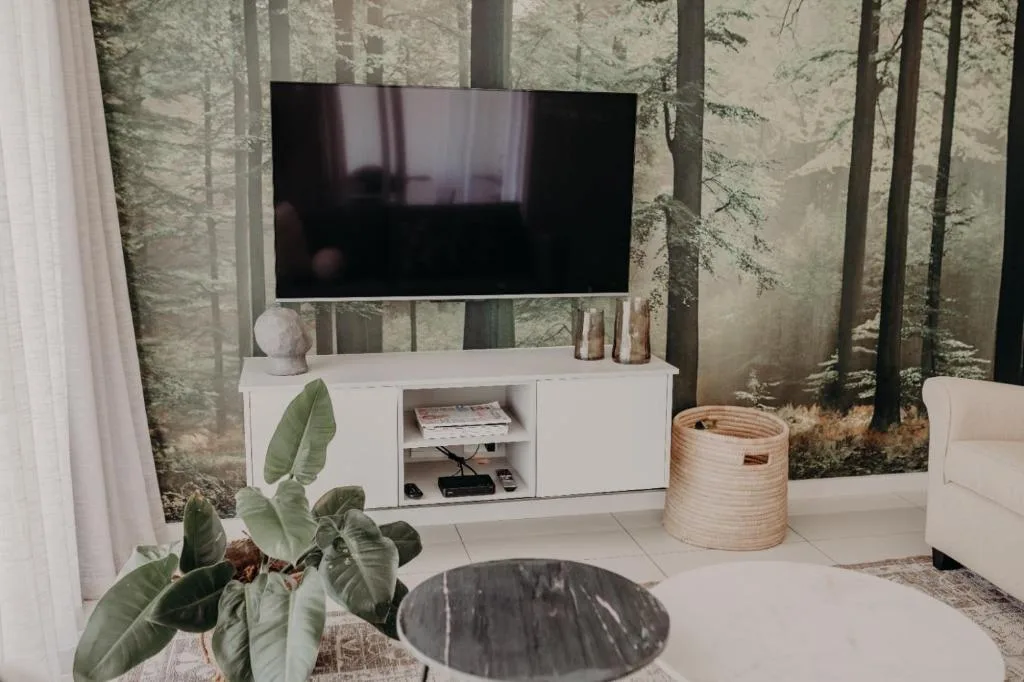 Modern living room with wall-mounted TV, white media console, forest wallpaper backdrop