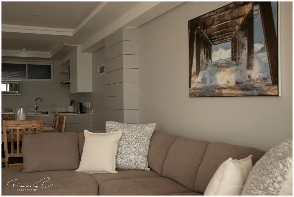 Open-plan lounge with taupe sofa, decorative pillows, and kitchen visible behind