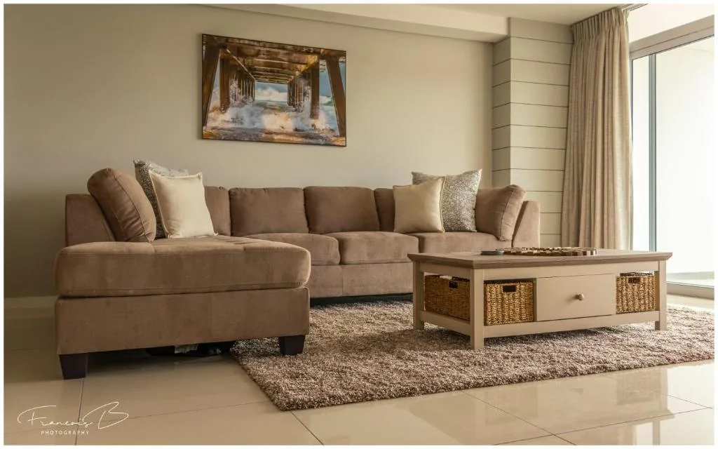 Modern lounge with beige sectional sofa, wooden coffee table, and large windows