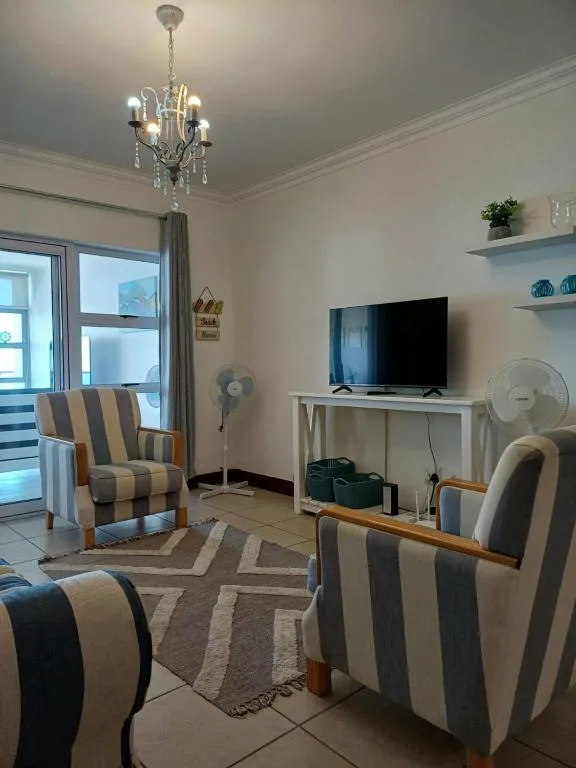 Modern living room with striped armchairs, TV, and elegant chandelier