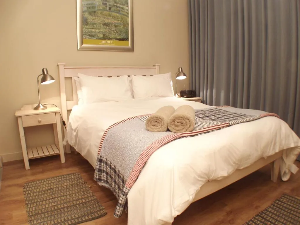 Freshly made bed with white linens, rolled towels, and patterned throw blanket