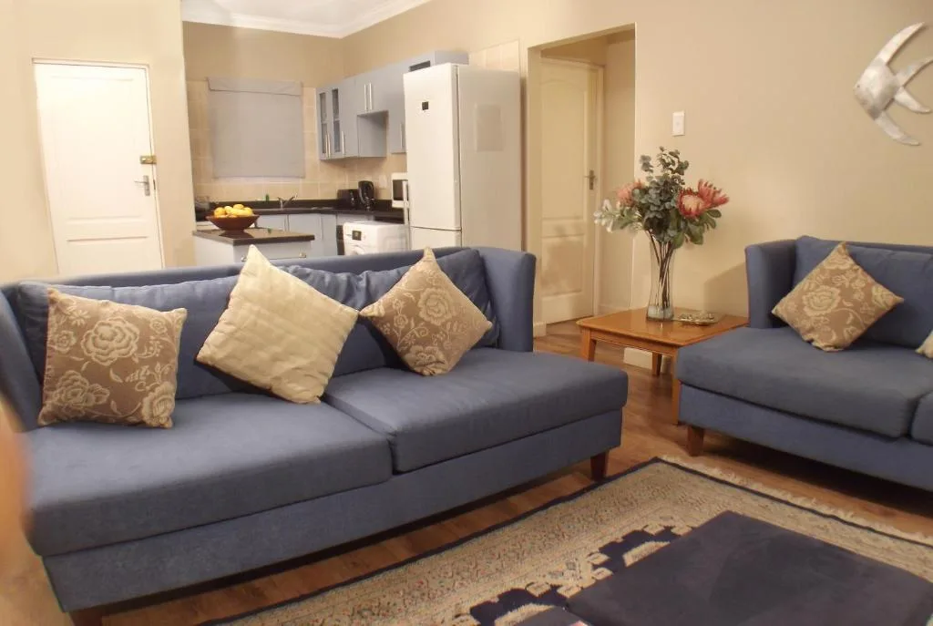 Open-plan living area with blue sofas, decorative pillows, and kitchen visible behind