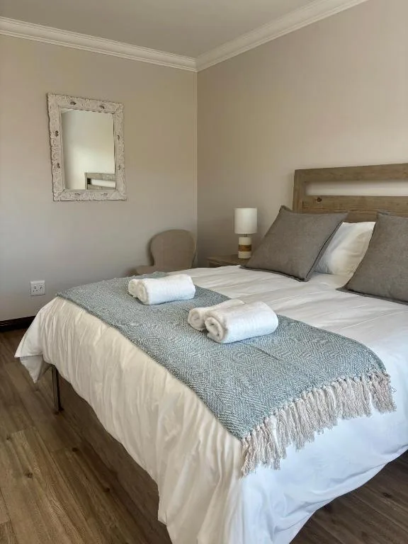Neatly made bed with gray throw and folded towels in light-filled bedroom