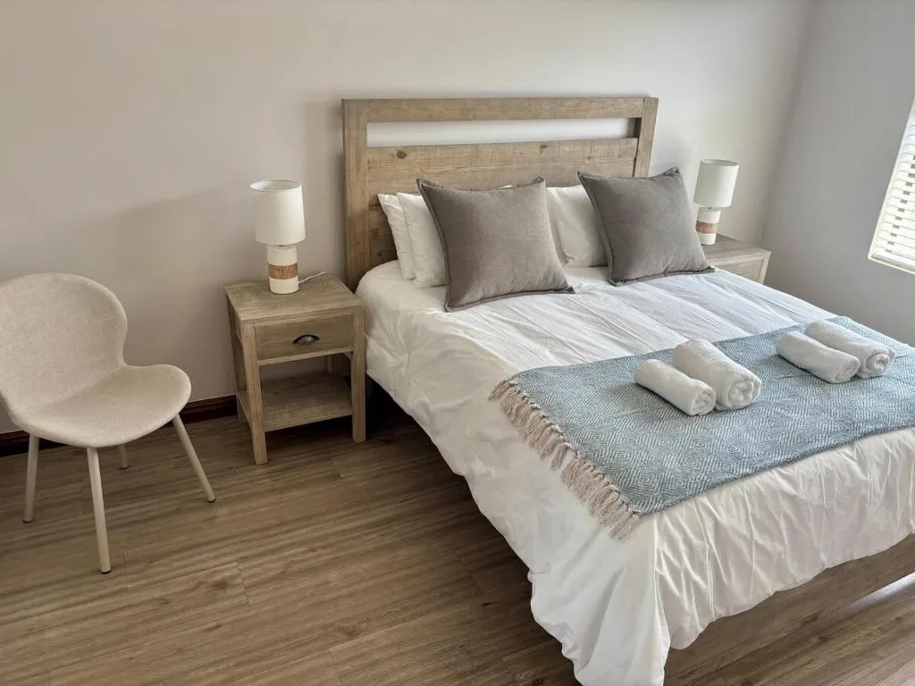 Bright bedroom with wooden bed frame, white linens, and rolled towels on display
